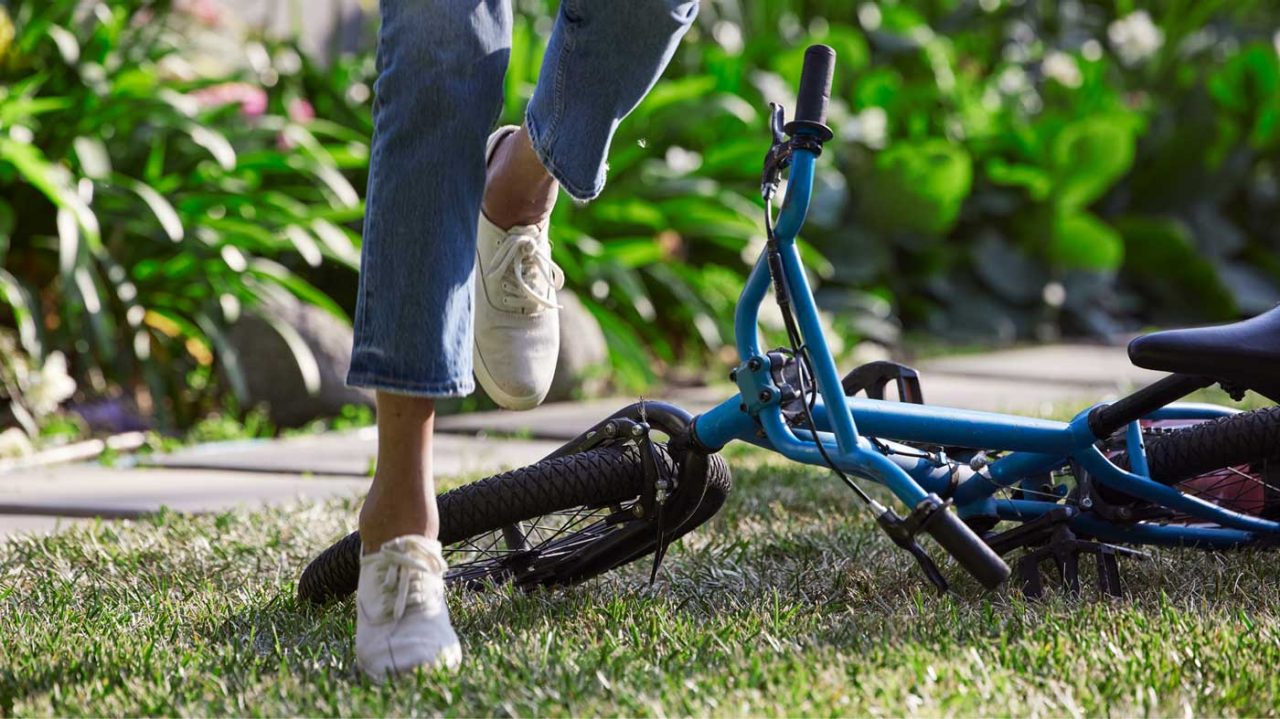 Legs stepping over a fallen bicycle on the ground.